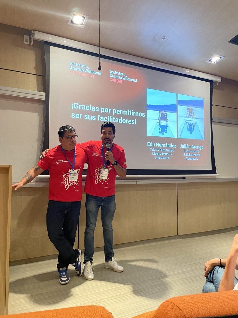Facilitadores del evento en el escenario con la pantalla de Techstars Startup Weekend Cali